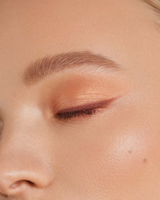 Model with light skin wearing EM Cosmetics Divine Skies in Faded Clementine for a soft, peachy orange eye look.