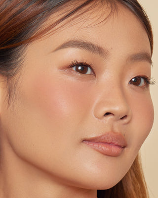 Model with medium skin wearing EM Cosmetics Pillow Plush Blush in Peanut for a natural look.