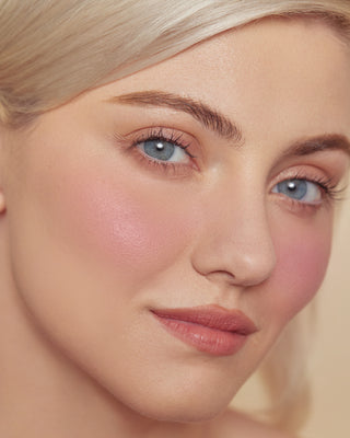 Model with light skin wearing EM Cosmetics Pillow Plush Blush in Tickled for a pink flush.