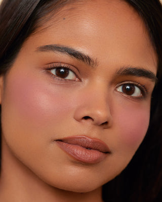 Model with deep skin wearing EM Cosmetics Pillow Plush Blush in Tickled.