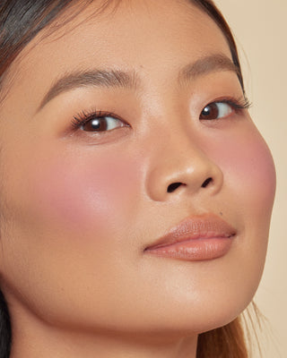 Model with medium skin wearing EM Cosmetics Pillow Plush Blush in Tickled.