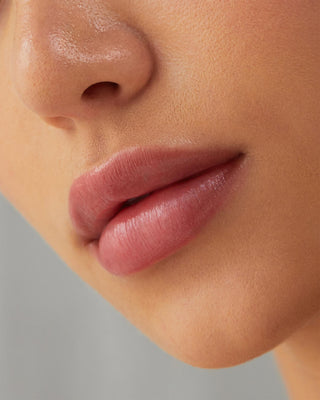 Model with light skin wearing EM Cosmetics Lip Cushion in Angele for a luminous pink tint.