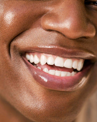 Model with dark skin wearing EM Cosmetics Lip Cushion in Clear Quartz for a high-shine, moisturized finish.