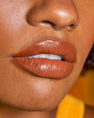 Model with dark skin wearing EM Cosmetics Lip Cushion in Faded Clementine for a luminous glow.