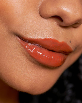 Model with medium skin wearing EM Cosmetics Lip Cushion in Faded Clementine for a glossy tint.