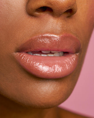Model with dark skin wearing EM Cosmetics Lip Cushion in Magic Hour for a sheer glossy finish.