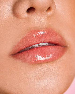 Model with medium skin wearing EM Cosmetics Lip Cushion in Magic Hour for a peachy tint.