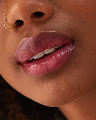 Model with dark skin wearing EM Cosmetics Lip Cushion in Mystic for a luminous berry tint.