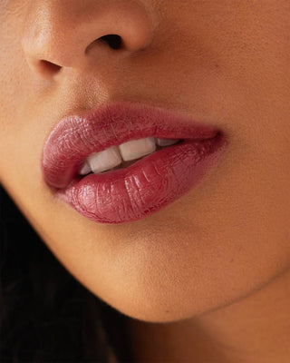 Model with medium skin wearing EM Cosmetics Lip Cushion in Mystic for a sheer berry tint.