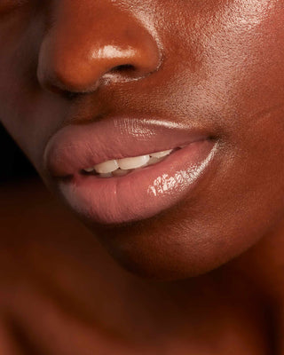 Model with dark skin wearing EM Cosmetics Lip Cushion in Venetian Rose for a sheer glossy finish.