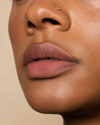 Model with medium skin wearing EM Cosmetics Phantom Blur Lip Tint in Monet for a soft, blurred cool-toned mauve finish.