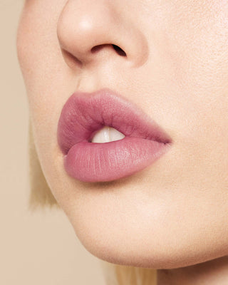 Model with medium skin wearing EM Cosmetics Phantom Blur Lip Tint in Odette, for a soft, blurred rosy mauve glow.