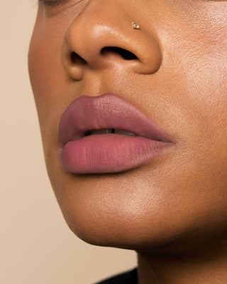 Model with medium skin wearing EM Cosmetics Phantom Blur Lip Tint in Odette, for a soft, blurred rosy mauve glow.
