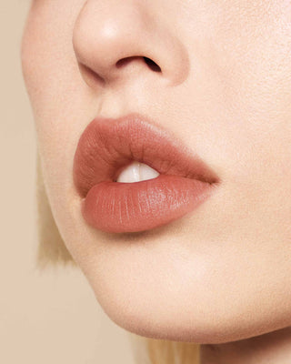 Model with medium skin wearing EM Cosmetics Phantom Blur Lip Tint in Sahar for a soft, warm rosy nude blurred finish.