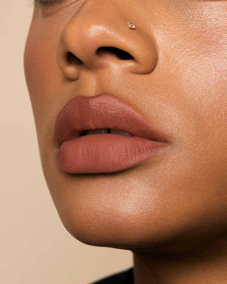 Model with medium skin wearing EM Cosmetics Phantom Blur Lip Tint in Sahar for a soft, warm rosy nude blurred finish.