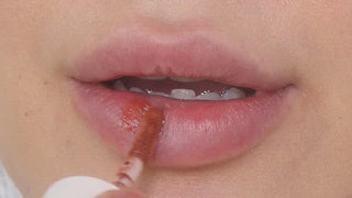 Model with dark skin wearing EM Cosmetics Everglass Lip Dew in Secret for a glossy, soft pink lip look.