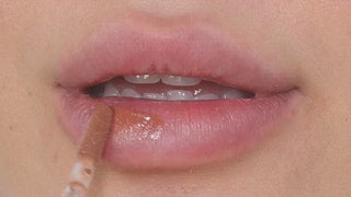 Model with dark skin wearing EM Cosmetics Everglass Lip Dew in Tea for a glossy, warm cocoa lip look.