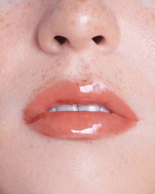 Model with dark skin wearing EM Cosmetics Everglass Lip Dew in Dream for a glossy, radiant clear lip look.