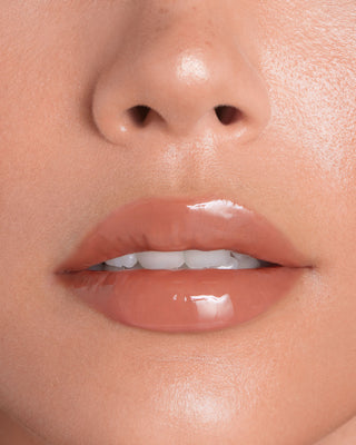 Model with dark skin wearing EM Cosmetics Everglass Lip Dew in Enchant for a glossy, rich berry lip look.