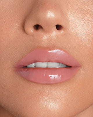 Model with dark skin wearing EM Cosmetics Everglass Lip Dew in Lullaby for a glossy, neutral rose lip look.