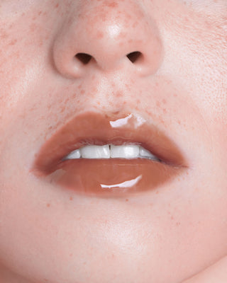 EM Cosmetics Everglass Lip Dew in Tea, a warm brown taupe shade, shown in its sleek, minimalist packaging.