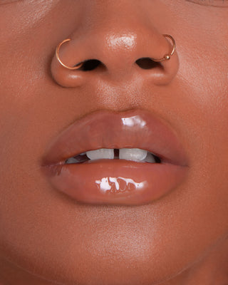 Model with medium skin wearing EM Cosmetics Everglass Lip Dew in Tea for a glossy, rosy taupe lip look.