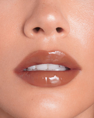 Model with light skin wearing EM Cosmetics Everglass Lip Dew in Tea for a glossy, neutral brown lip look.