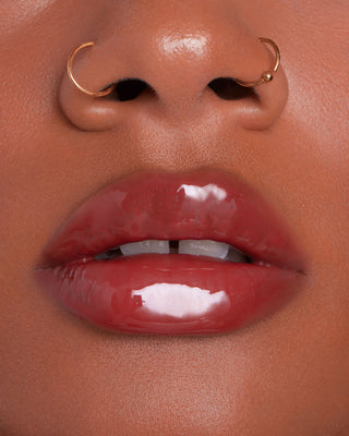 Model with medium skin wearing EM Cosmetics Everglass Lip Dew in Temptress for a glossy, muted berry lip look.