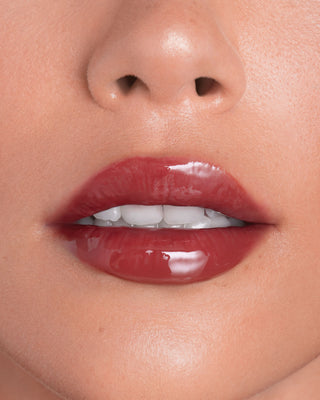 Model with light skin wearing EM Cosmetics Everglass Lip Dew in Temptress for a glossy, vibrant berry lip look.