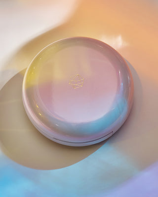 Stylized product shot of EM Cosmetics Moonbeam Cushion Highlighter in Divinity in its white compact.