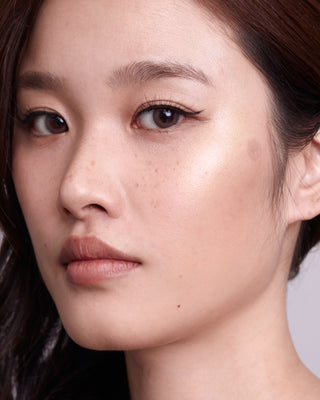 Model with medium skin wearing EM Cosmetics Moonbeam Cushion Highlighter in Halo for a warm, radiant highlight.