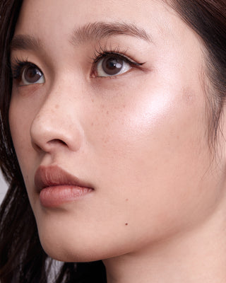 Model with medium skin wearing EM Cosmetics Moonbeam Cushion Highlighter in Aura for a radiant, pink-toned highlight.
