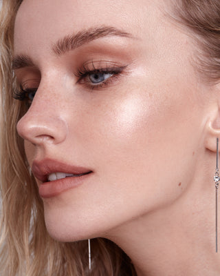 Model with light skin wearing EM Cosmetics Moonbeam Cushion Highlighter in Aura for a soft, rosy glow.