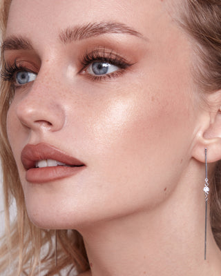 Model with light skin wearing EM Cosmetics Moonbeam Cushion Highlighter in Halo for a sun-kissed golden glow.