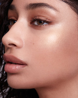 Model with medium skin wearing EM Cosmetics Moonbeam Cushion Highlighter in Divinity for a radiant champagne glow.