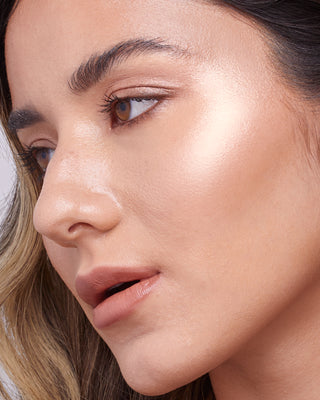 Model with medium skin wearing EM Cosmetics Sunscape Highlighter in Clarity for a soft, champagne highlight.