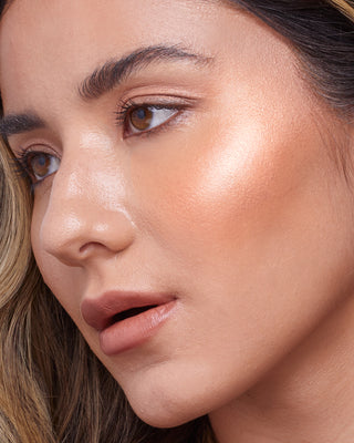 Model with medium skin wearing EM Cosmetics Sunscape Highlighter in Majesty for a warm, bronzed radiance.