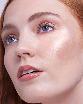 Model with light skin wearing EM Cosmetics Sunscape Highlighter in Clarity for a bright, wet-look radiance.