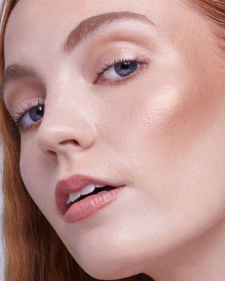 Model with light skin wearing EM Cosmetics Sunscape Highlighter in Legendary for a bright, golden radiance.