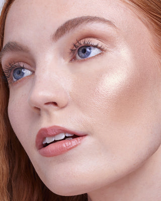 Model with light skin wearing EM Cosmetics Sunscape Highlighter in Majesty for a sun-kissed, bronze glow.