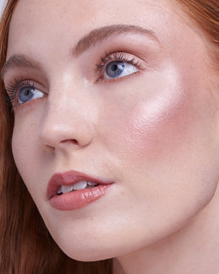 Model with light skin wearing EM Cosmetics Sunscape Highlighter in Serenity for a soft, pinkish radiance.