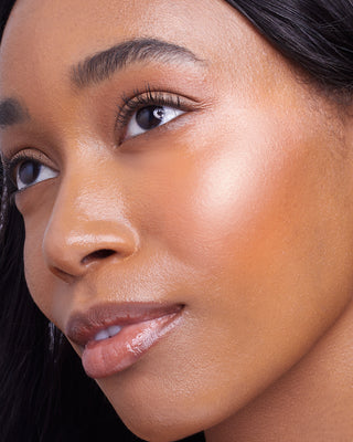 Model with dark skin wearing EM Cosmetics Sunscape Highlighter in Majesty for a luminous, rich gold highlight.